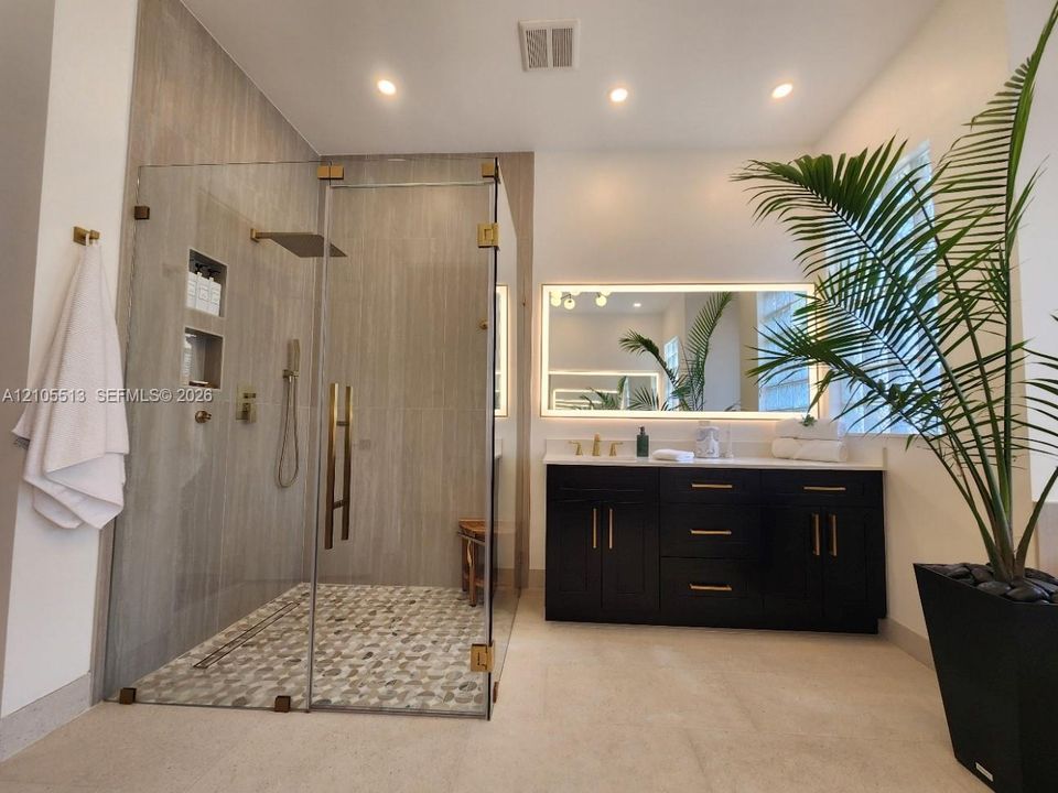 Expansive walk-in shower with frameless glass enclosure, gold-tone fixtures, and integrated wall niches