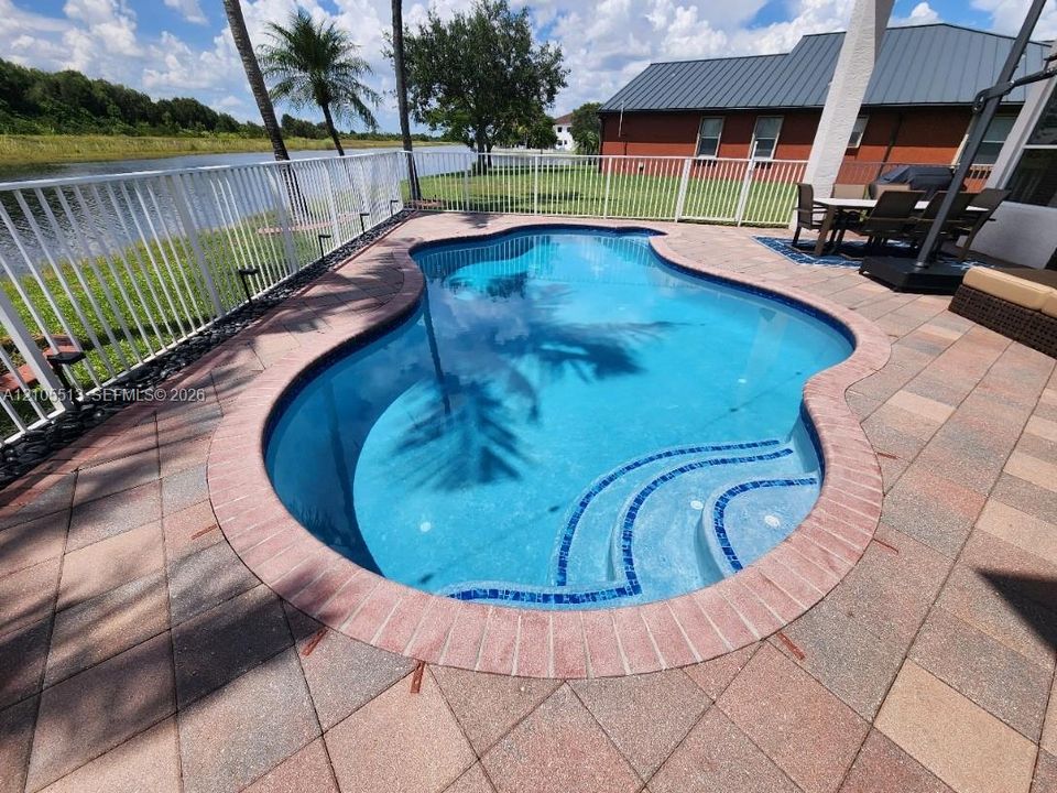 Newly resurfaced saltwater freeform swimming pool with auto cleaning system,  integrated steps, brick coping, and a paver patio