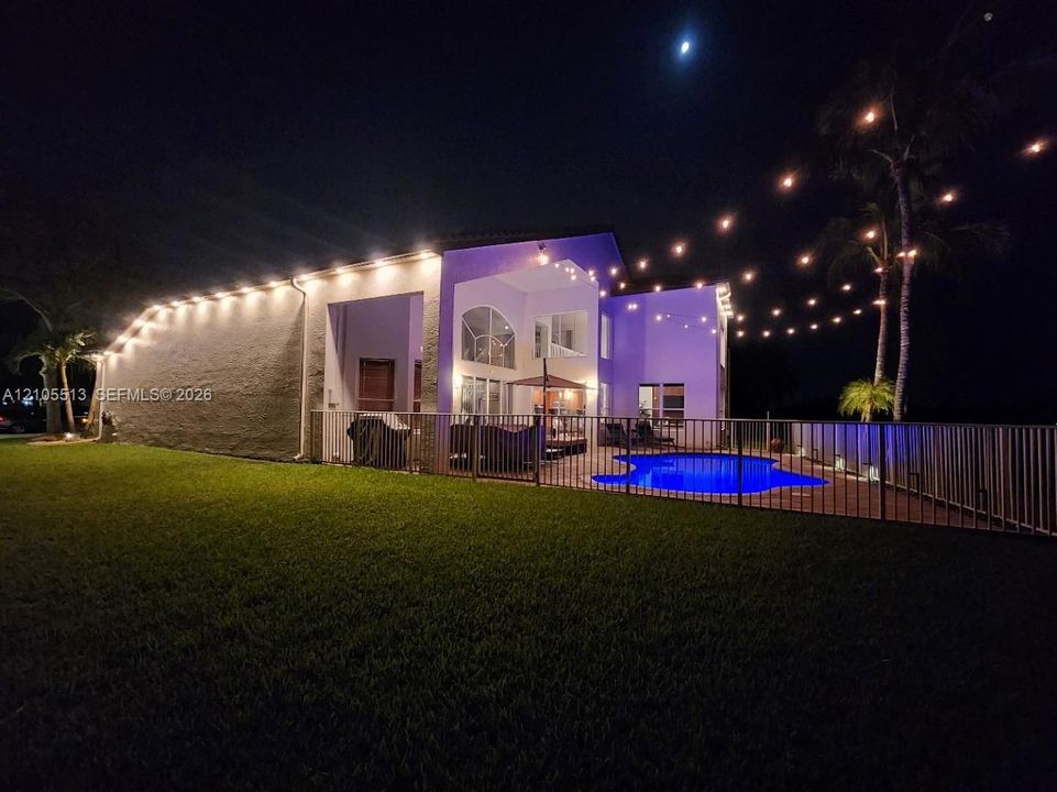Night view of side with automated security down lighting, low voltage string lights & multi-colored pool light