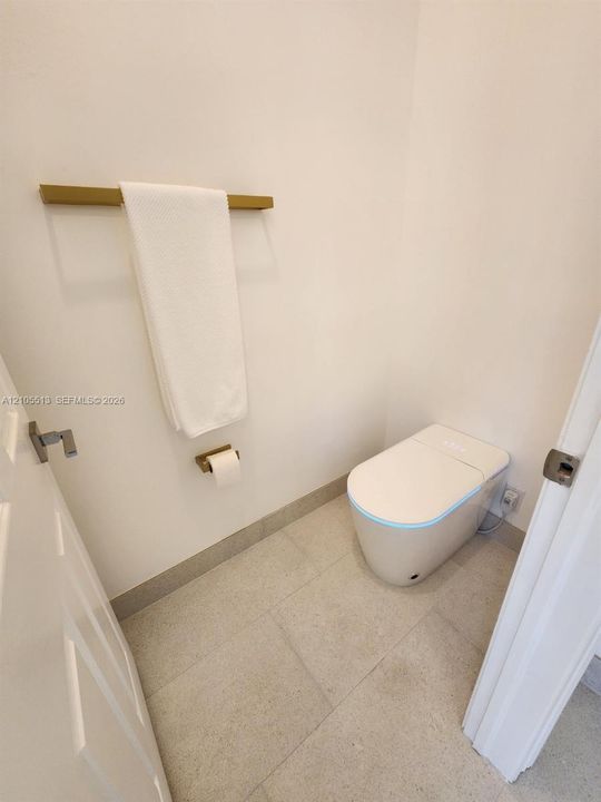 White walls with a modern smart toilet, porcelain flooring, and  matching gold-finish fixtures