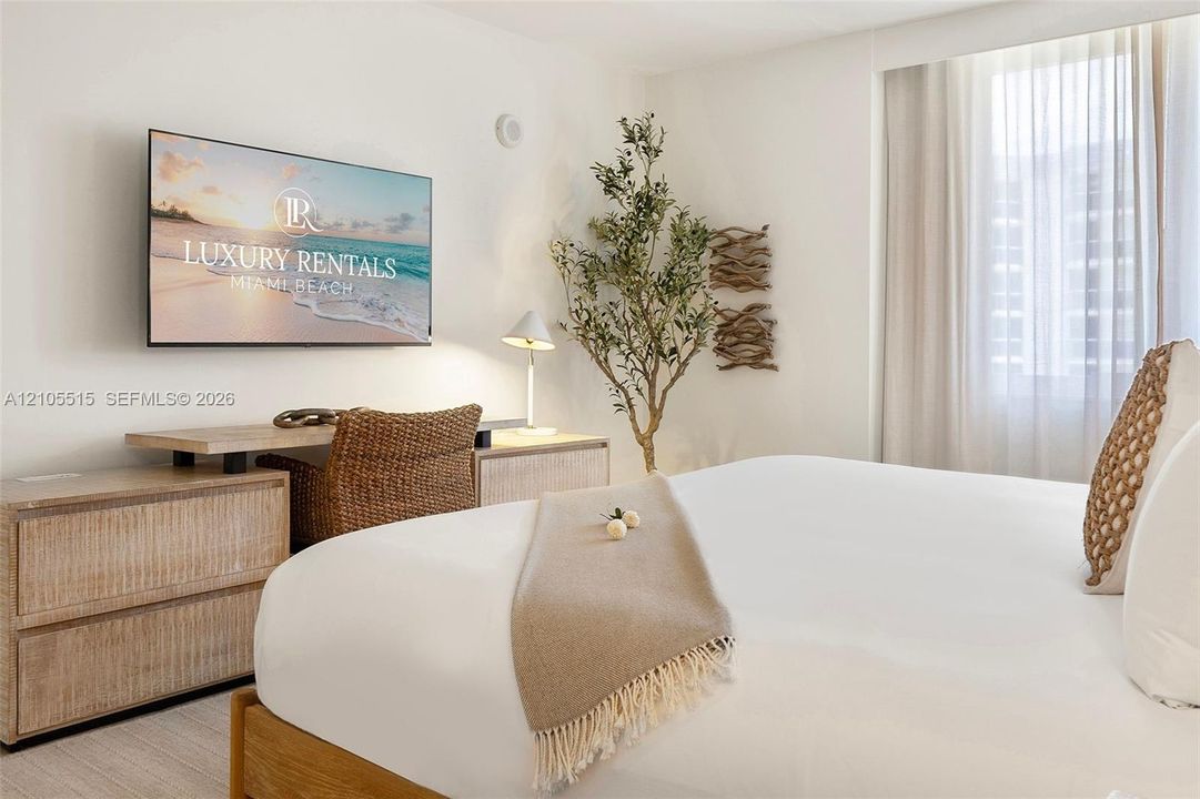 Neutral-toned room featuring a large floor-to-ceiling window dressed with sheer curtains and light wood-finish flooring