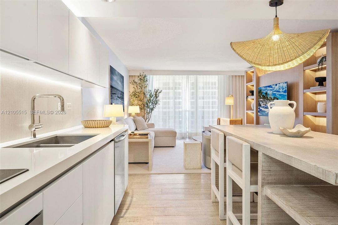 Contemporary kitchen featuring white flat-panel cabinetry, light-toned stone countertops, integrated under-cabinet lighting, wood-finish flooring, and built-in floor-to-ceiling shelving