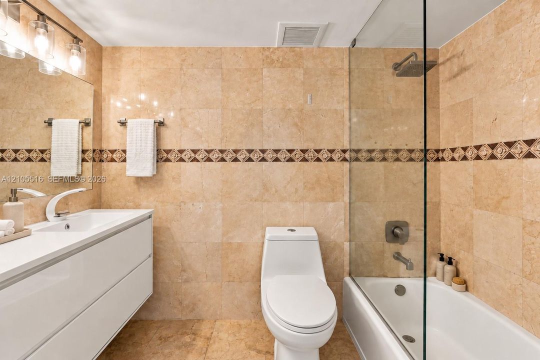 Bathroom featuring full-height stone-finish wall tile, a frameless glass shower panel, a wall-mounted vanity with integrated sink, and a modern light fixture