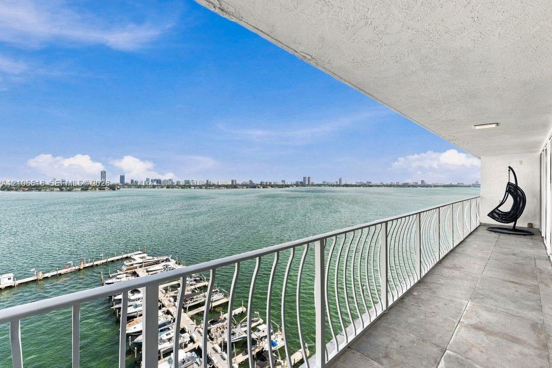 Expansive balcony with wide water frontage, city skyline, marina, and white railing with decorative curves
