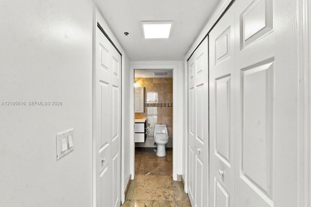 Hallway with white panel doors, overhead square light fixture, and tile flooring