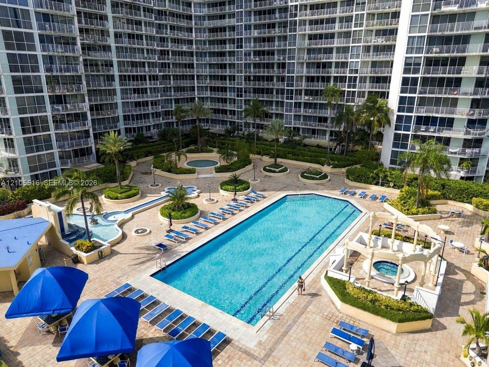 Expansive outdoor amenity deck featuring a rectangular swimming pool, multiple lounging areas, mature landscaping, and a covered hot tub