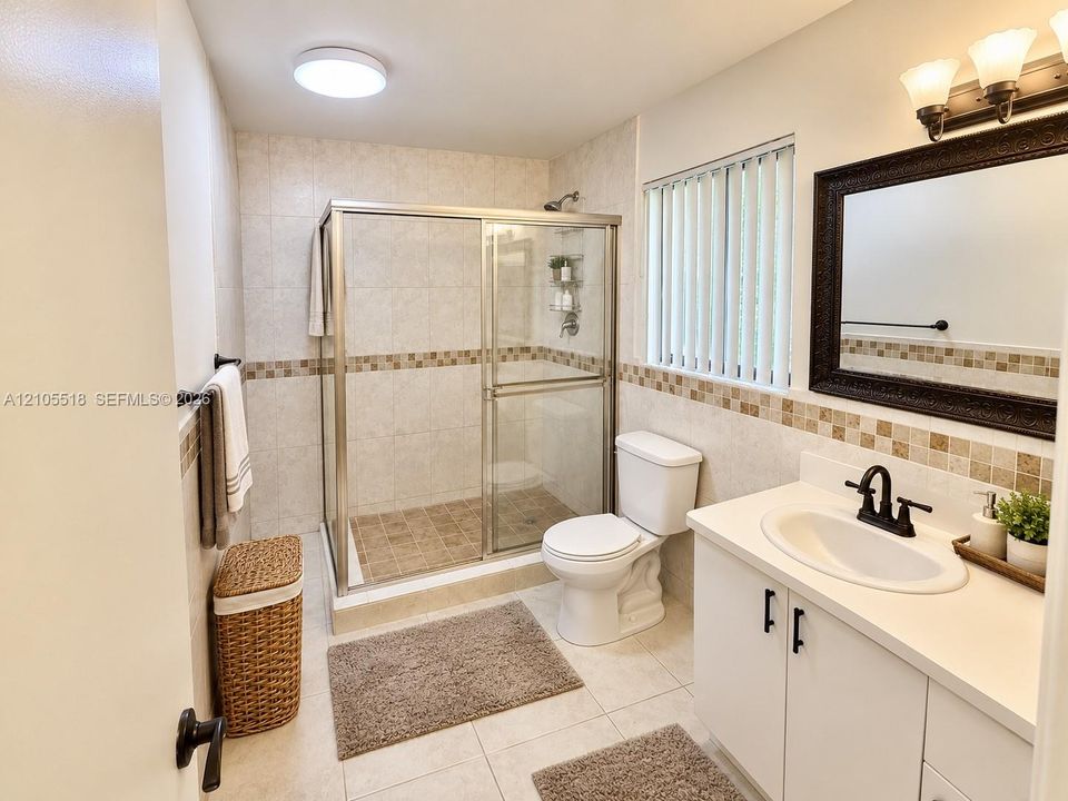 Bathroom featuring a walk-in shower with glass enclosure, white vanity cabinet, solid-surface countertop with integrated sink, tile wall accents, and vanity lighting