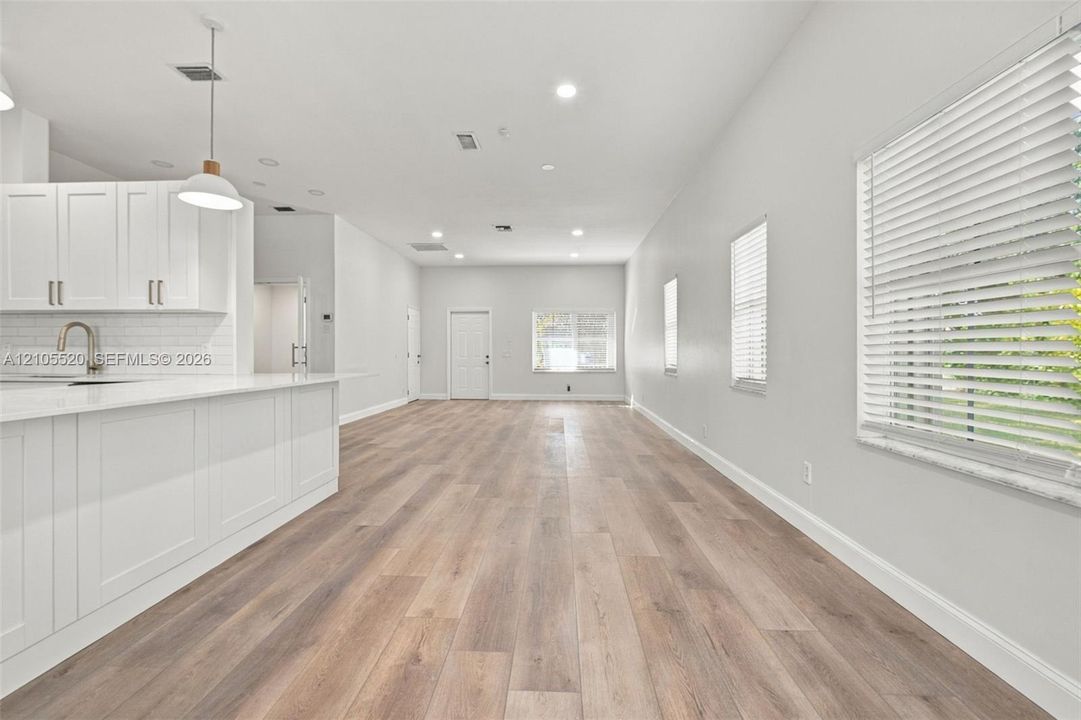 Open-concept interior featuring wood-finish flooring, white shaker-style cabinetry, a quartz-topped island, recessed lighting, and horizontal window blinds