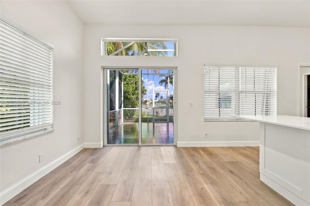 Interior space featuring wood-finish flooring, white walls, horizontal window blinds, sliding glass patio door with a transom window, and a built-in white kitchen peninsula