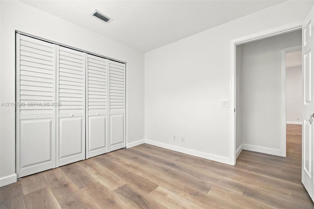 Neutral-toned room featuring wood-finish flooring, white walls, and a four-panel bi-fold closet with louvered doors