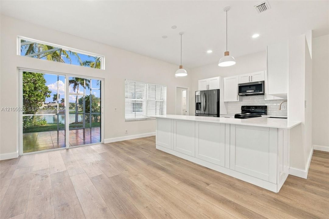 Kitchen featuring a quartz-topped island, white cabinetry, wood-finish flooring, recessed lighting, and sliding glass doors with a transom window
