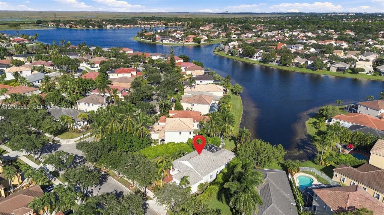Aerial perspective of a residential property featuring a screen-enclosed pool, mature palm trees, and proximity to a community lake
