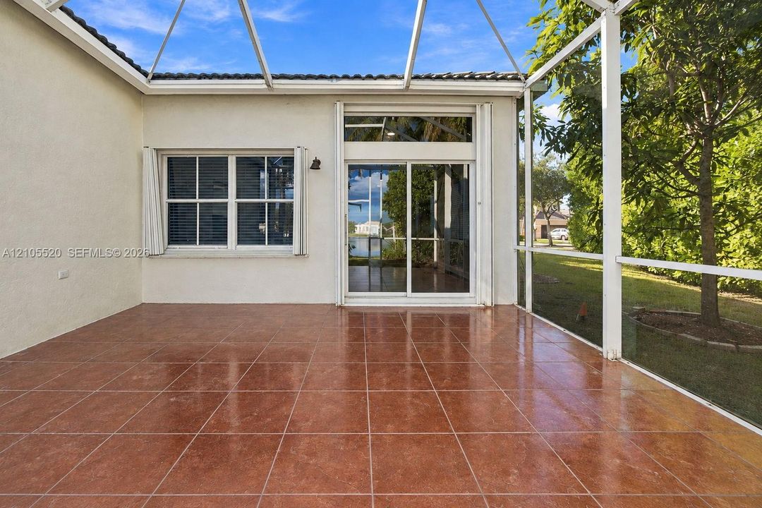 Screened-in lanai featuring tile flooring, sliding glass doors with a transom window, and white metal framing