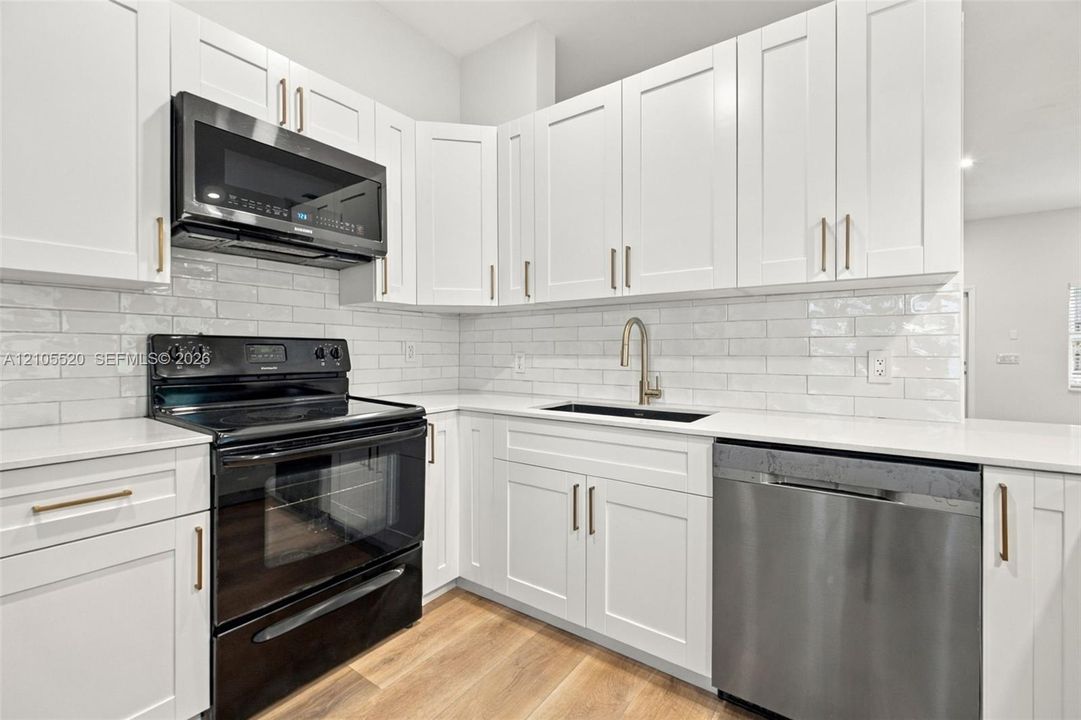 Kitchen featuring shaker-style cabinetry, quartz countertops, subway tile backsplash, stainless steel appliances, and wood-finish flooring