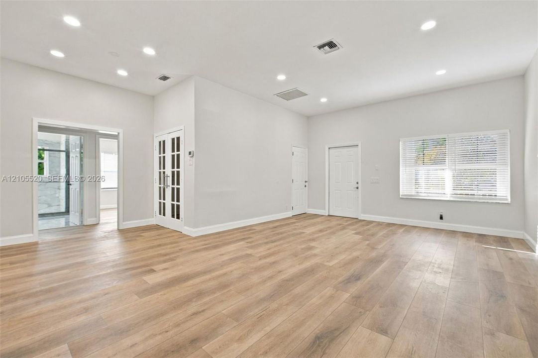 Open-concept room featuring wood-finish flooring, recessed lighting, white French doors with glass panels, and large windows with horizontal blinds