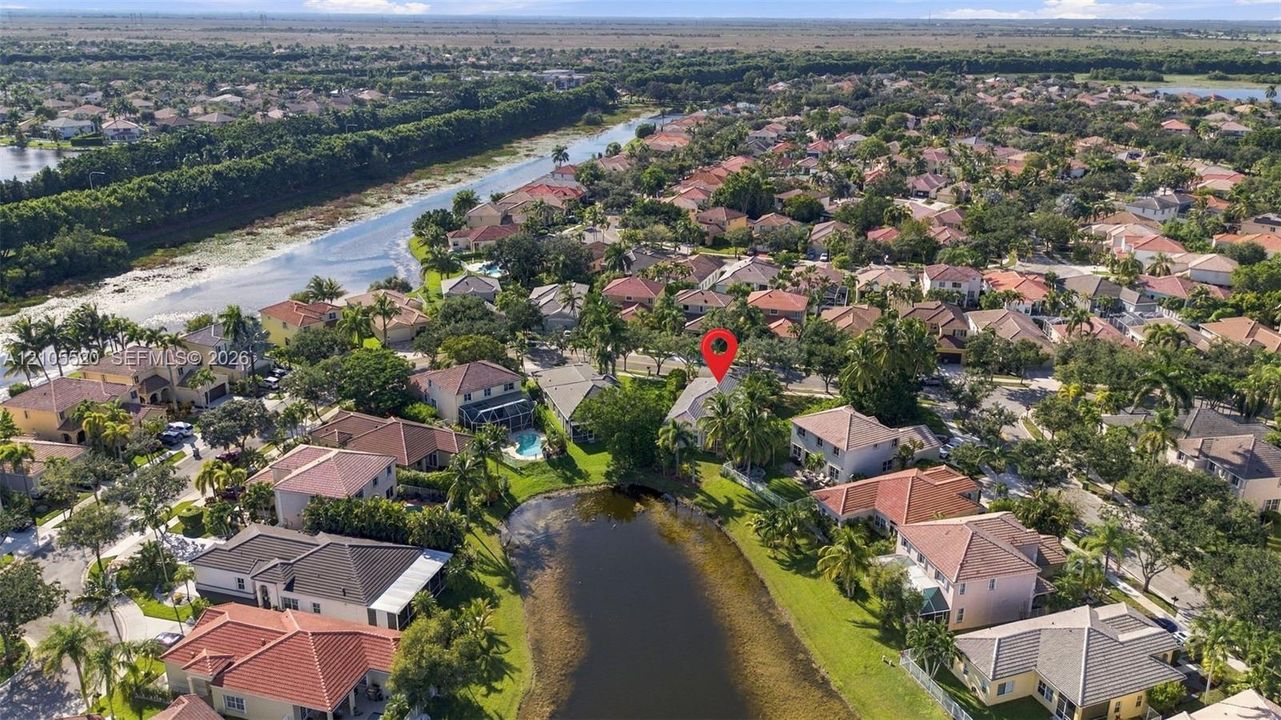 Aerial perspective of a multi-story residence featuring a tile roof, situated on a lot bordering a community pond with mature landscaping and palm trees
