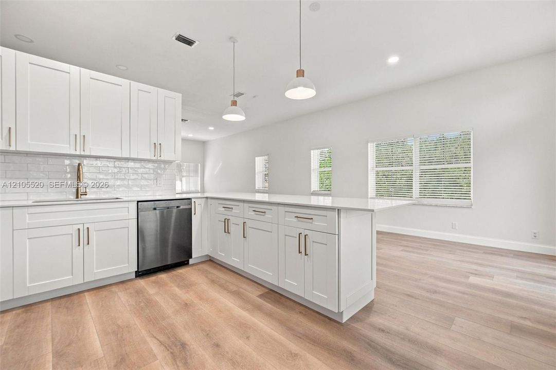 Kitchen featuring white shaker-style cabinetry, quartz countertops, a stainless steel dishwasher, subway tile backsplash, and wood-finish flooring