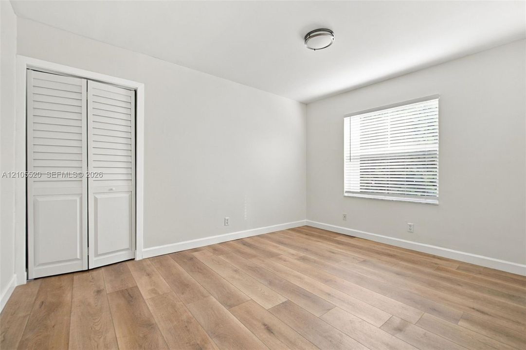 Interior room featuring wood-finish flooring, neutral wall paint, a double-panel louvered closet door, a single-window configuration with horizontal blinds, and a flush-mount ceiling light fixture