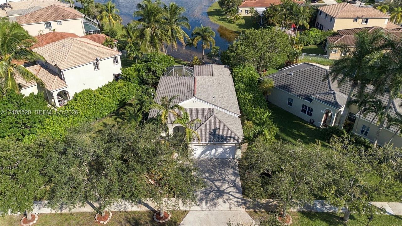 Aerial perspective featuring a concrete tile roof, paved driveway, enclosed rear patio, and mature landscaping on a waterfront lot