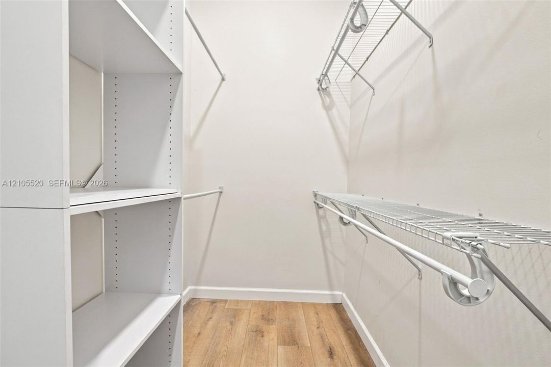 Walk-in storage space featuring wood-finish flooring, white laminate shelving towers, and white wire rack shelving with integrated hanging rods