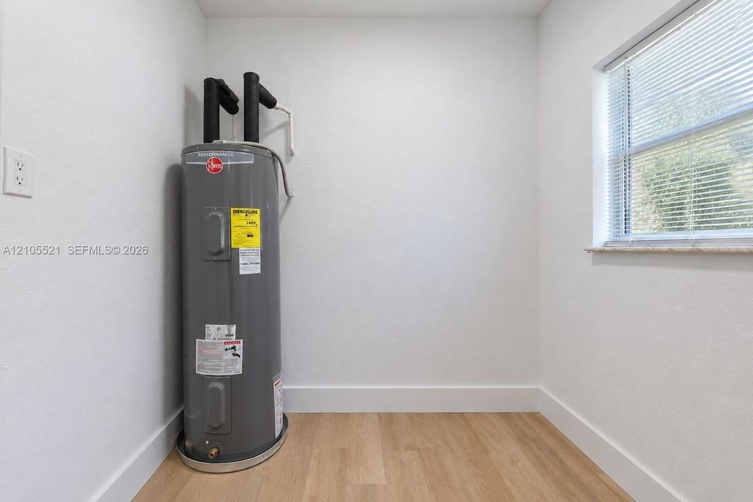Water heater, wood-finish flooring, white walls, window with blinds, and white trim