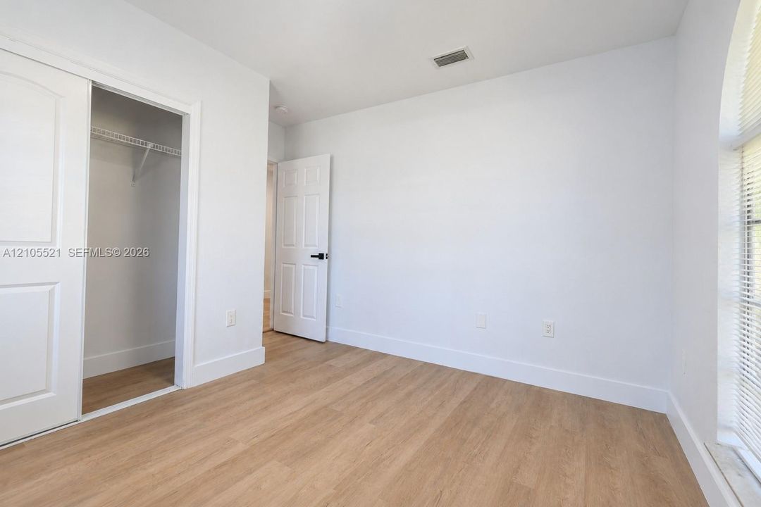 Wood-finish flooring, white walls, white trim, sliding closet doors, and a window with blinds