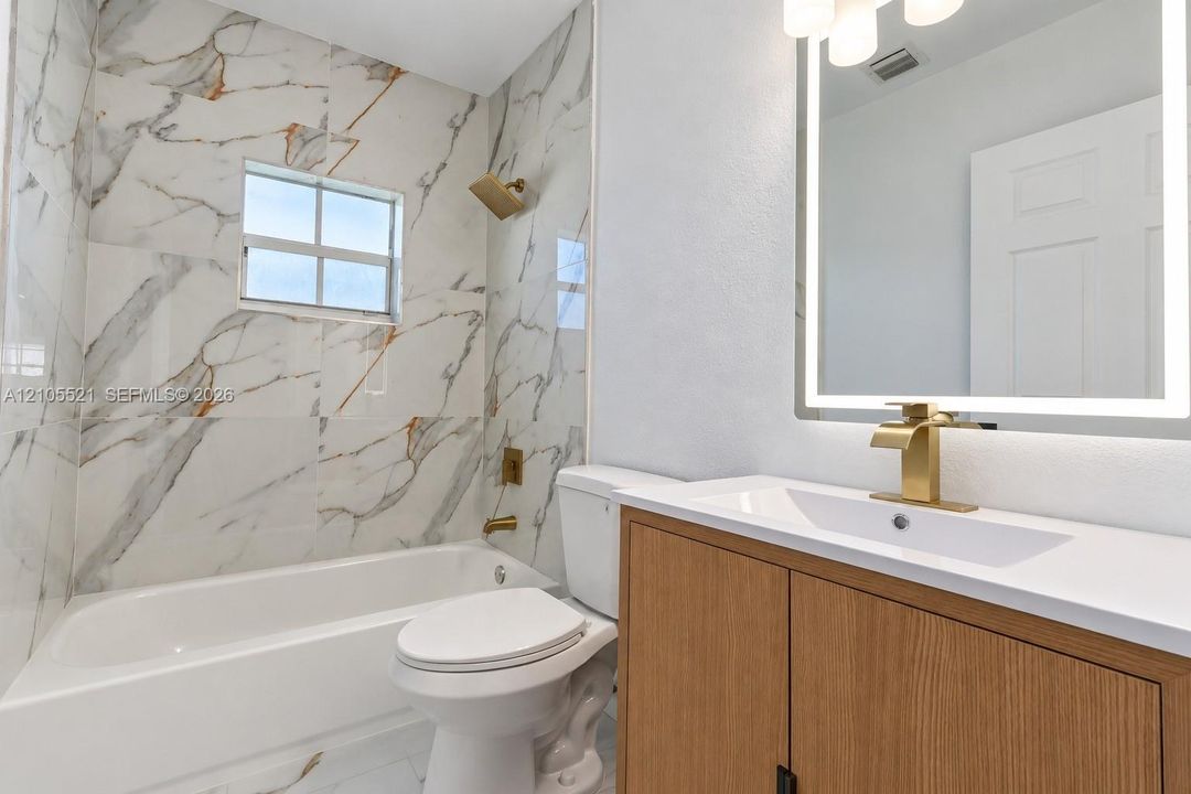 Bathroom featuring large format marble-look wall tile, a built-in bathtub, a vanity with wood-finish cabinetry, a white countertop, and a lighted mirror