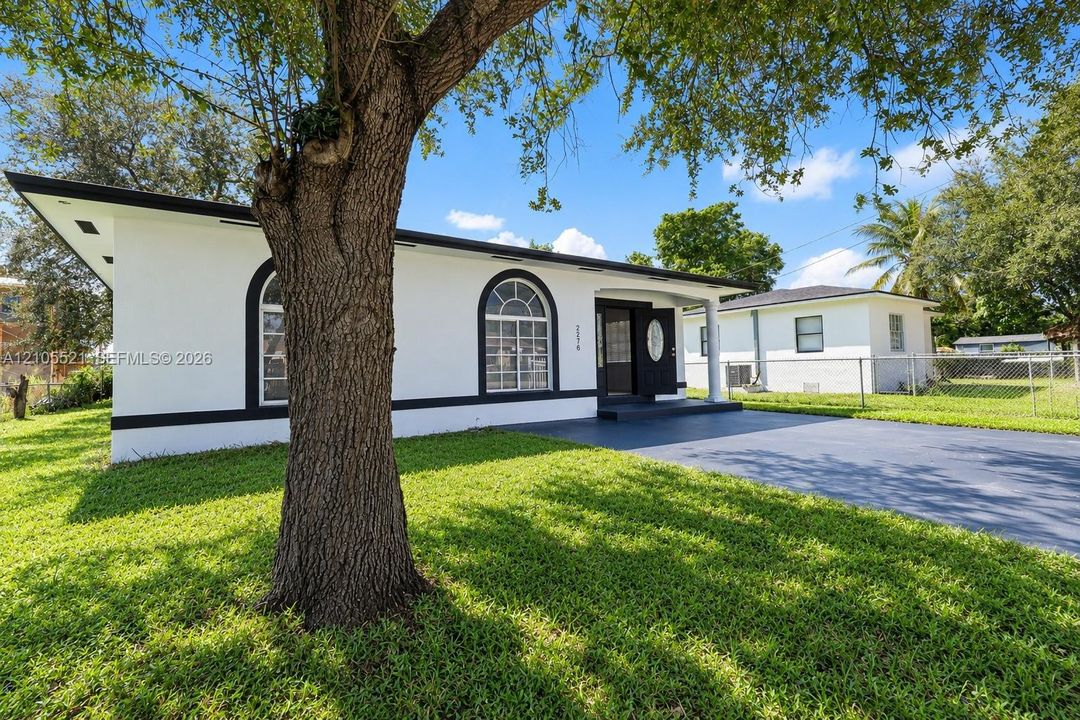 White exterior with black trim, arched windows, covered entry, and a paved driveway