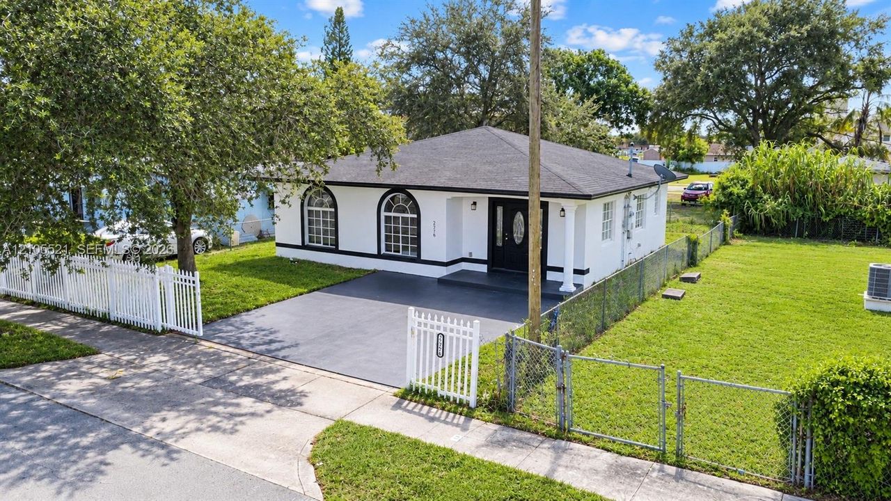White exterior with black trim, arched windows, covered entry, black asphalt driveway, and a white picket fence