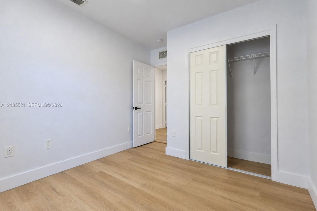 Light wood-finish flooring with white baseboards, a white paneled door with a black handle, and a white sliding closet door