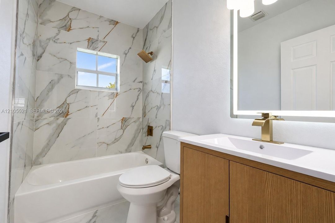 Bathroom featuring a single vanity with wood-finish cabinetry, a white countertop, and a lighted mirror