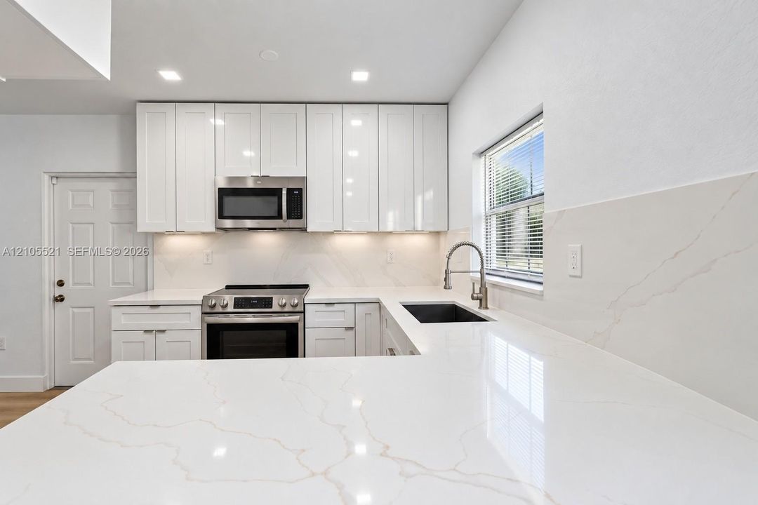 White shaker-style cabinetry with under-cabinet lighting, stainless steel appliances, and a stainless steel sink with a gooseneck faucet
