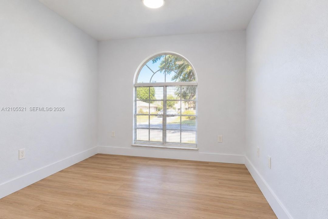 Arched window with blinds, wood-finish flooring, white walls, and a ceiling light fixture