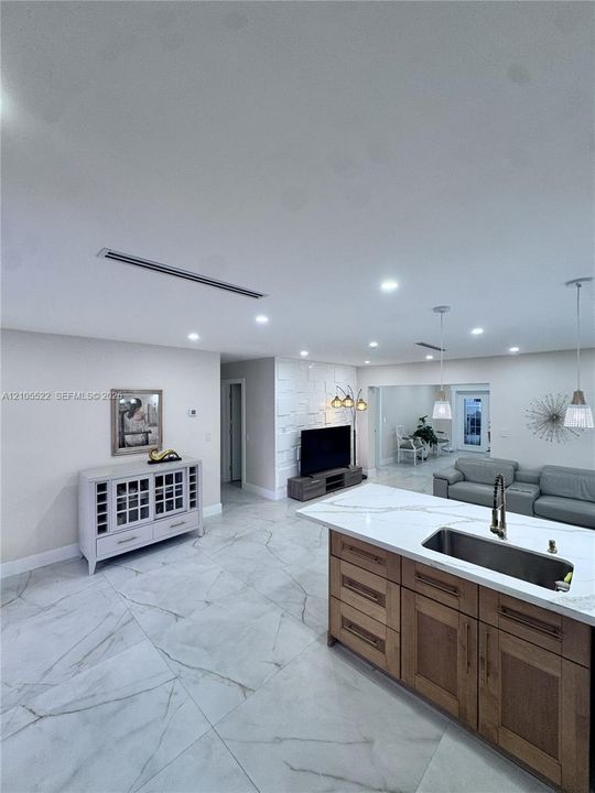 Open-concept layout with recessed lighting, large format tile flooring, a kitchen island with integrated sink, and a textured accent wall