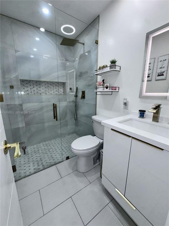 Glass-enclosed shower with a rainfall showerhead, integrated shower niche, and mosaic tile flooring