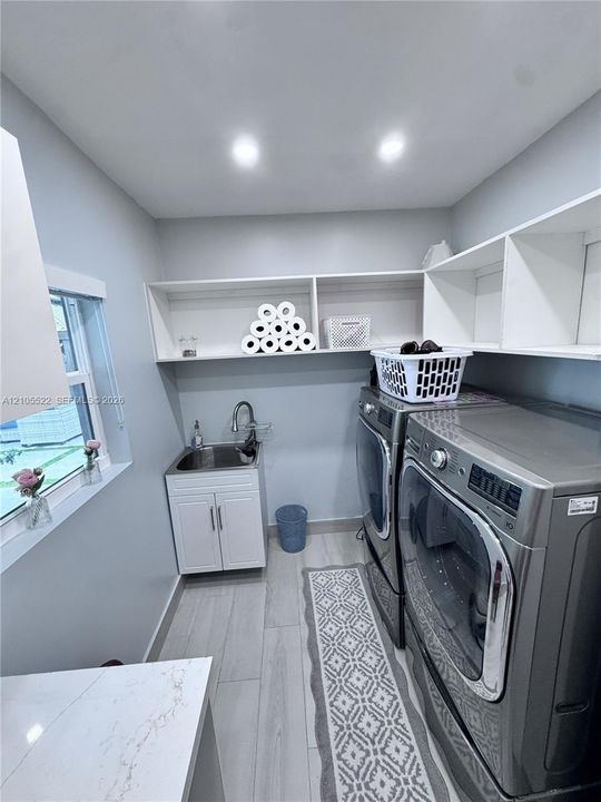 Laundry space featuring wood-finish flooring, built-in shelving, a utility sink with cabinetry, and a window