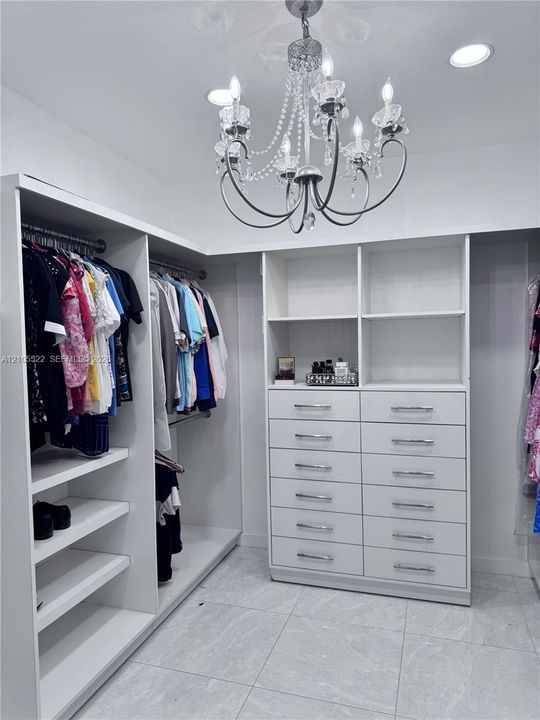 Built-in closet system featuring white shelving, multiple hanging rods, and an integrated dresser with chrome pulls