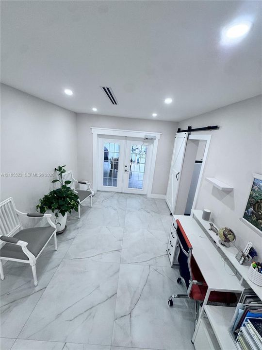Recessed lighting illuminates the space, featuring large format tile flooring and white french doors