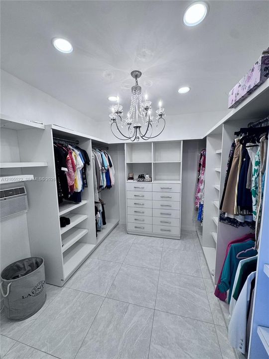 Walk-in closet featuring extensive built-in shelving, integrated drawers, recessed lighting, a central chandelier, and large format floor tiles