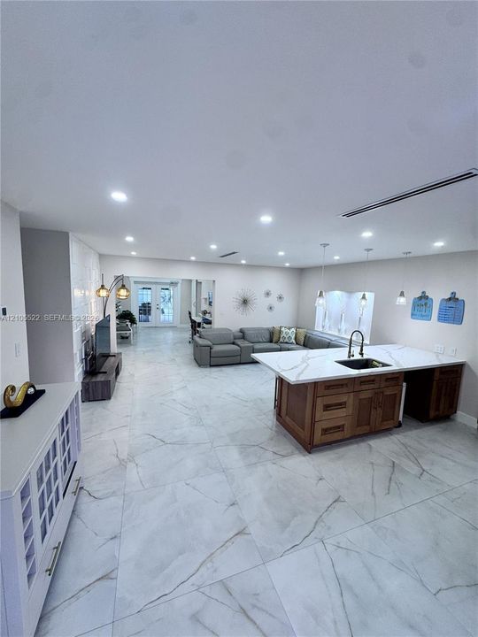 Open-concept living space with large format tile flooring, recessed lighting, and a kitchen island featuring a black sink and faucet