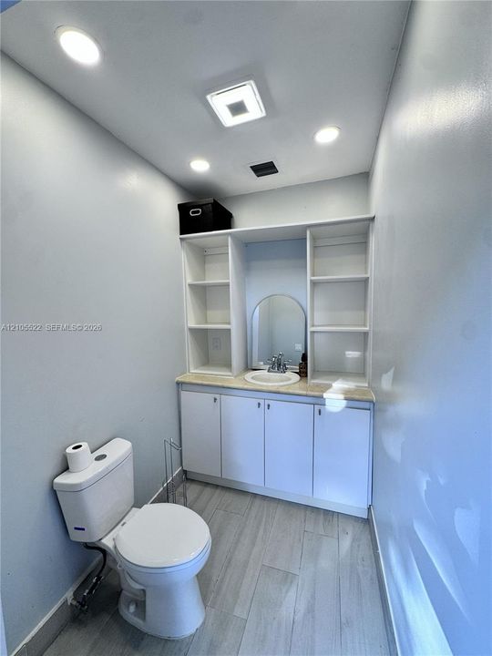 Recessed lighting, wood-finish flooring, white vanity with integrated sink, white storage cabinetry, and built-in shelving