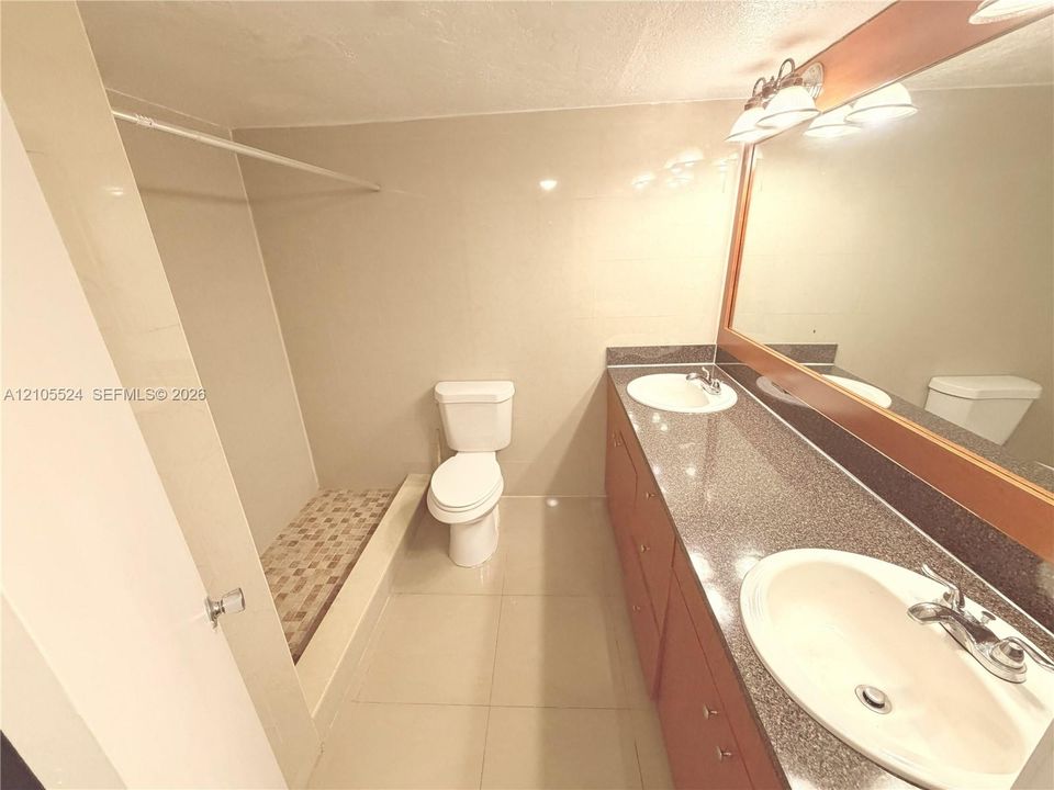 Dual vanity with integrated sinks, wood-finish cabinetry, a large mirrored wall, and a three-light fixture