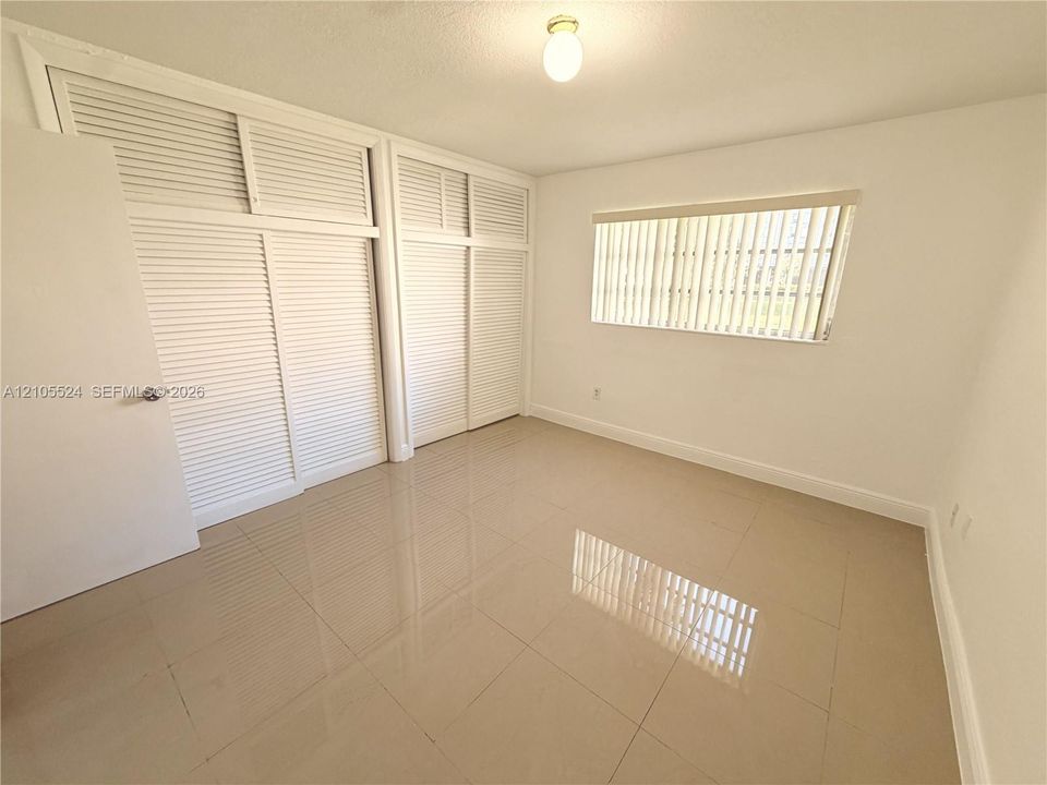 Spacious interior featuring louvered closet doors, a single window with blinds, and polished tile flooring