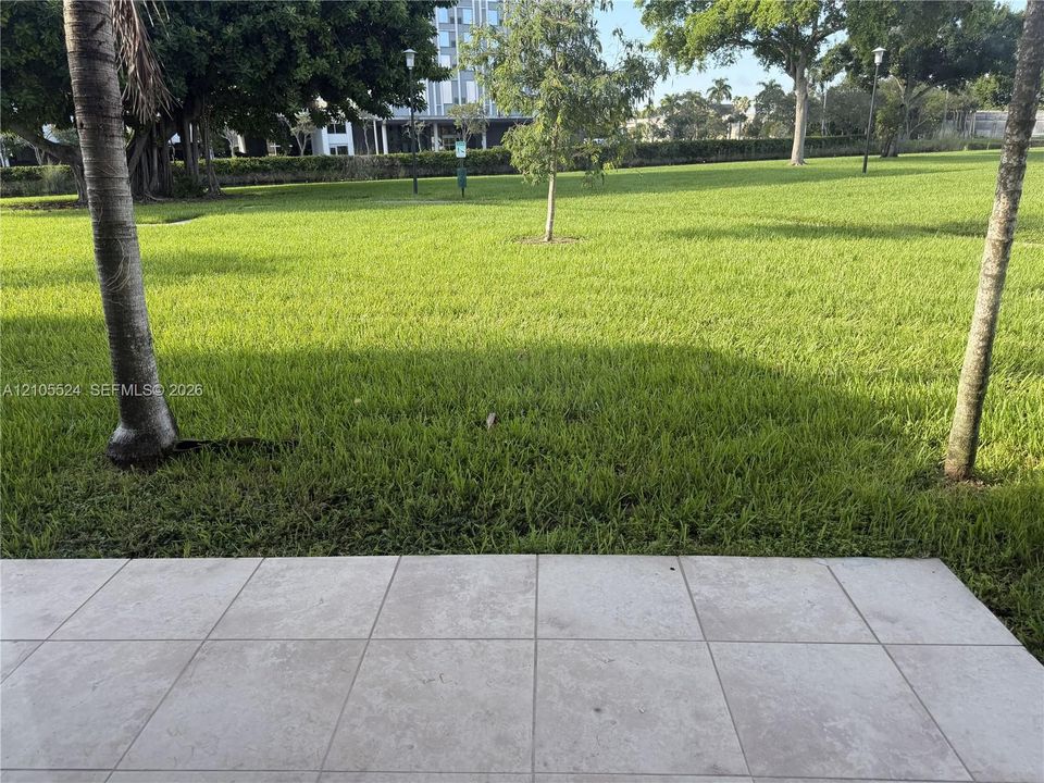 Tiled patio with a manicured lawn, established trees, and building structures in the background