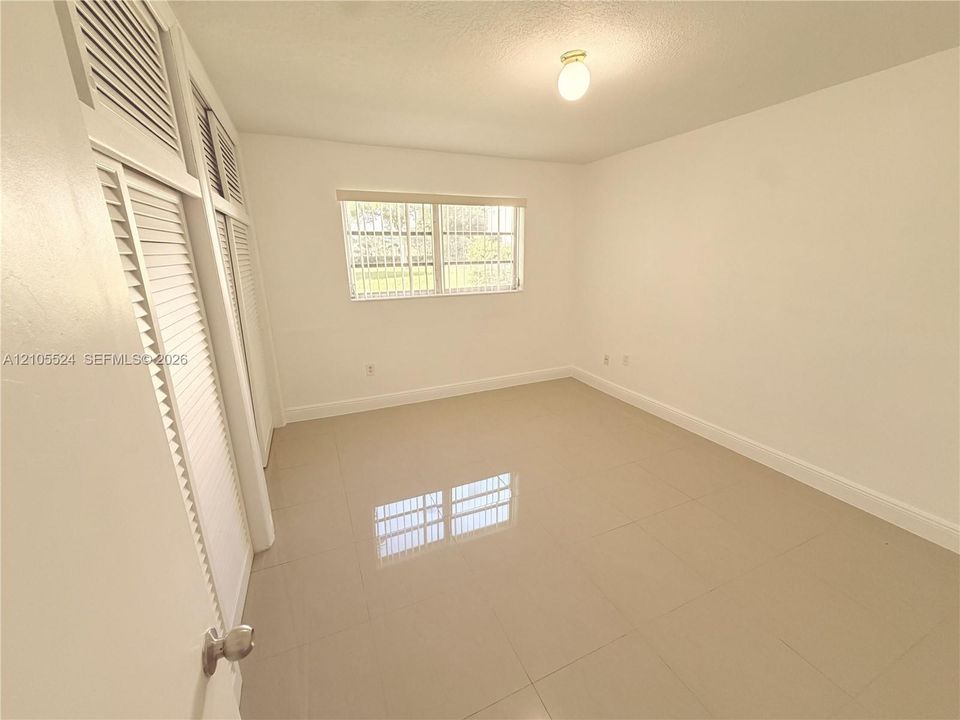 White walls, tile flooring, window with vertical blinds, and louvered bifold closet doors
