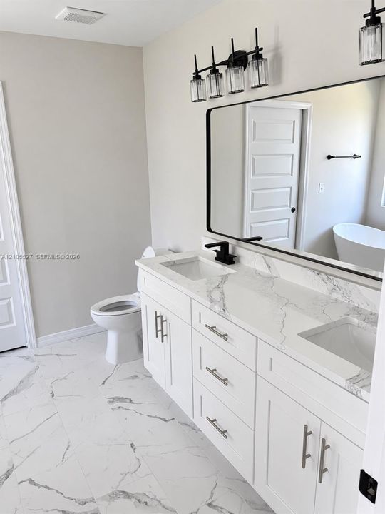 Dual vanity with white cabinetry and integrated sinks, complemented by a large framed mirror and a four-light fixture