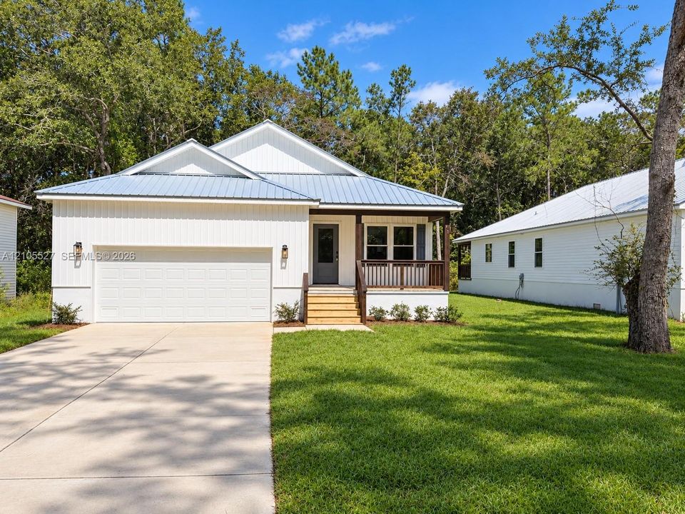 Contemporary exterior with white vertical siding, blue metal roof, covered front porch, attached garage, and a concrete driveway