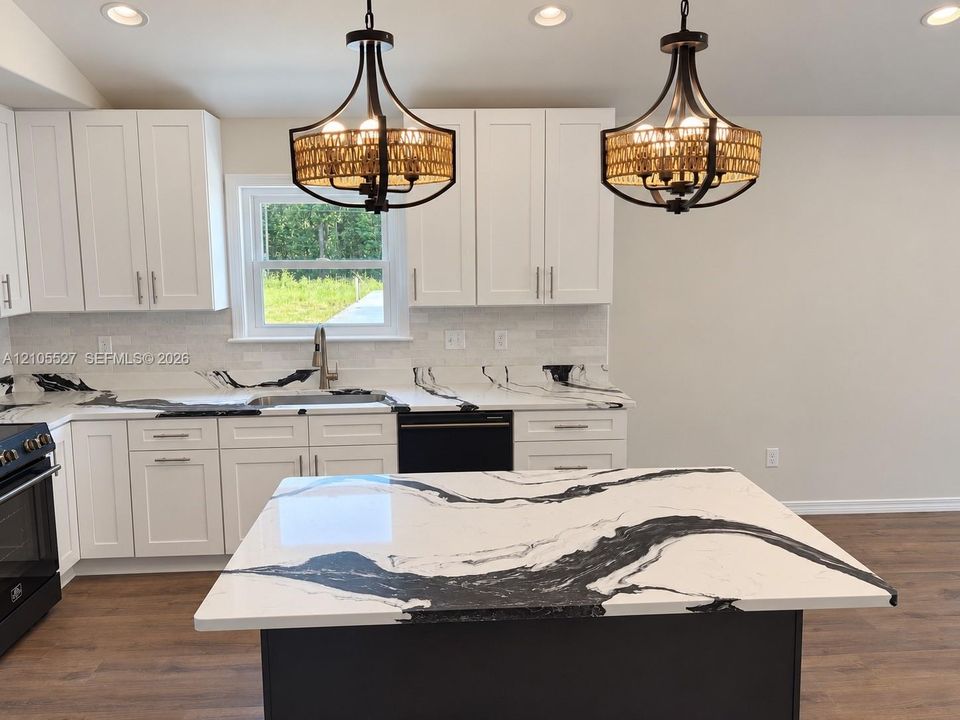 White shaker-style cabinetry, patterned countertops, wood-finish flooring, and recessed and pendant lighting