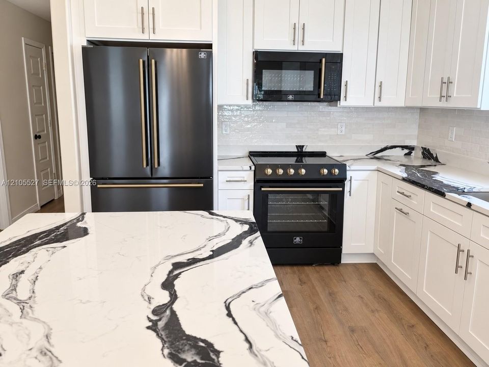 White shaker cabinetry with matte black appliances, wood-finish flooring, and a patterned countertop