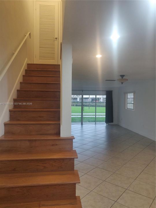 Wood-finish staircase with white handrail, recessed lighting, and tile flooring